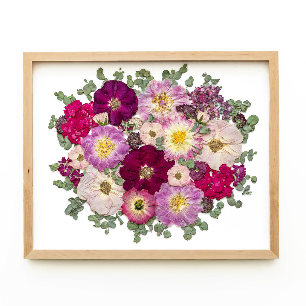A natural wood frame showcasing a stunning arrangement of preserved flowers. Soft pink and vibrant red roses entwine with elegant pink dahlias, creating a captivating display of colors and textures. The natural wood frame complements the organic beauty of the preserved flowers, adding a touch of rustic charm to the composition. The combination of pink and red hues evokes a sense of romance and beauty, making this arrangement a delightful visual treat.