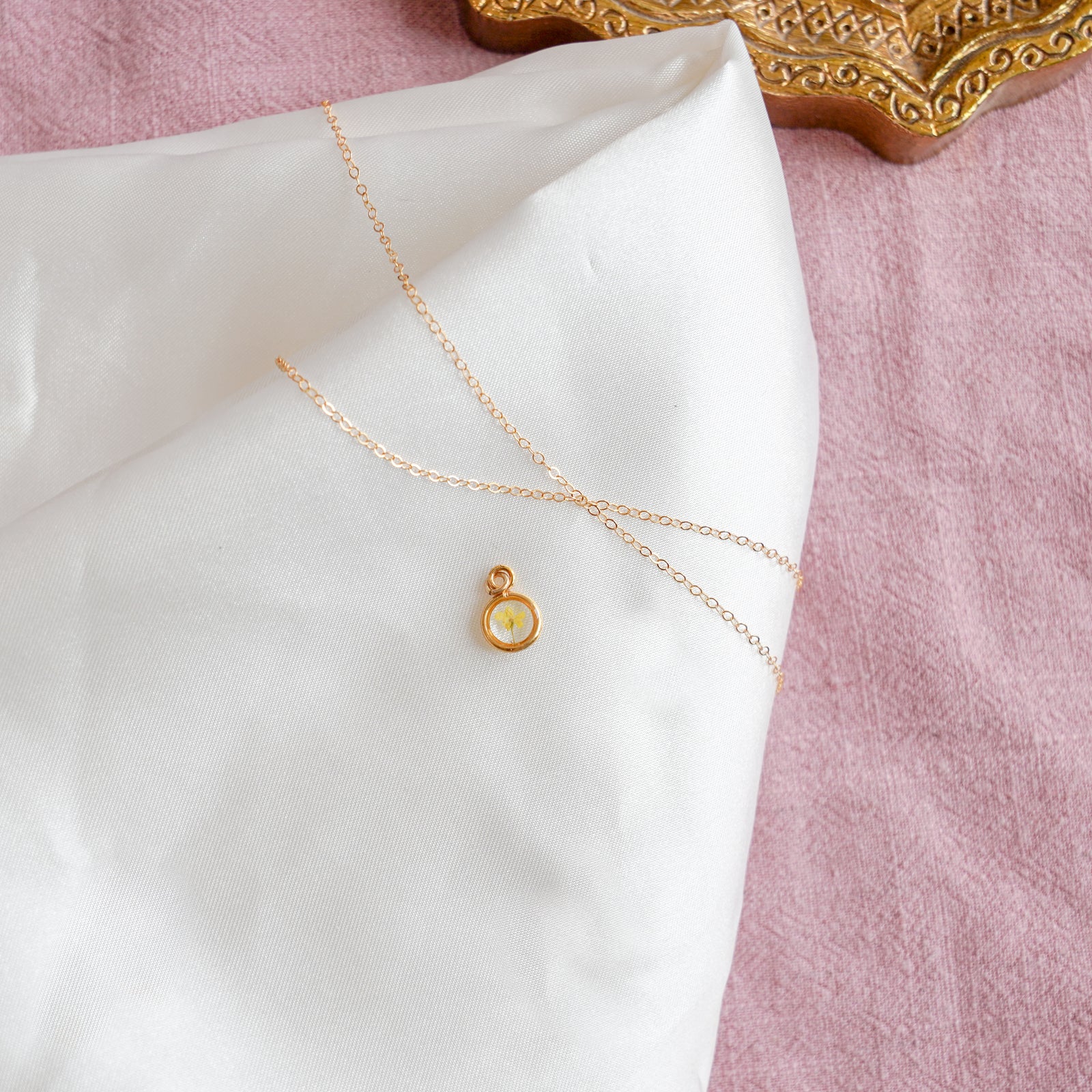 Pressed Floral's March birth flower charm 18K gold plated on a white and pink background