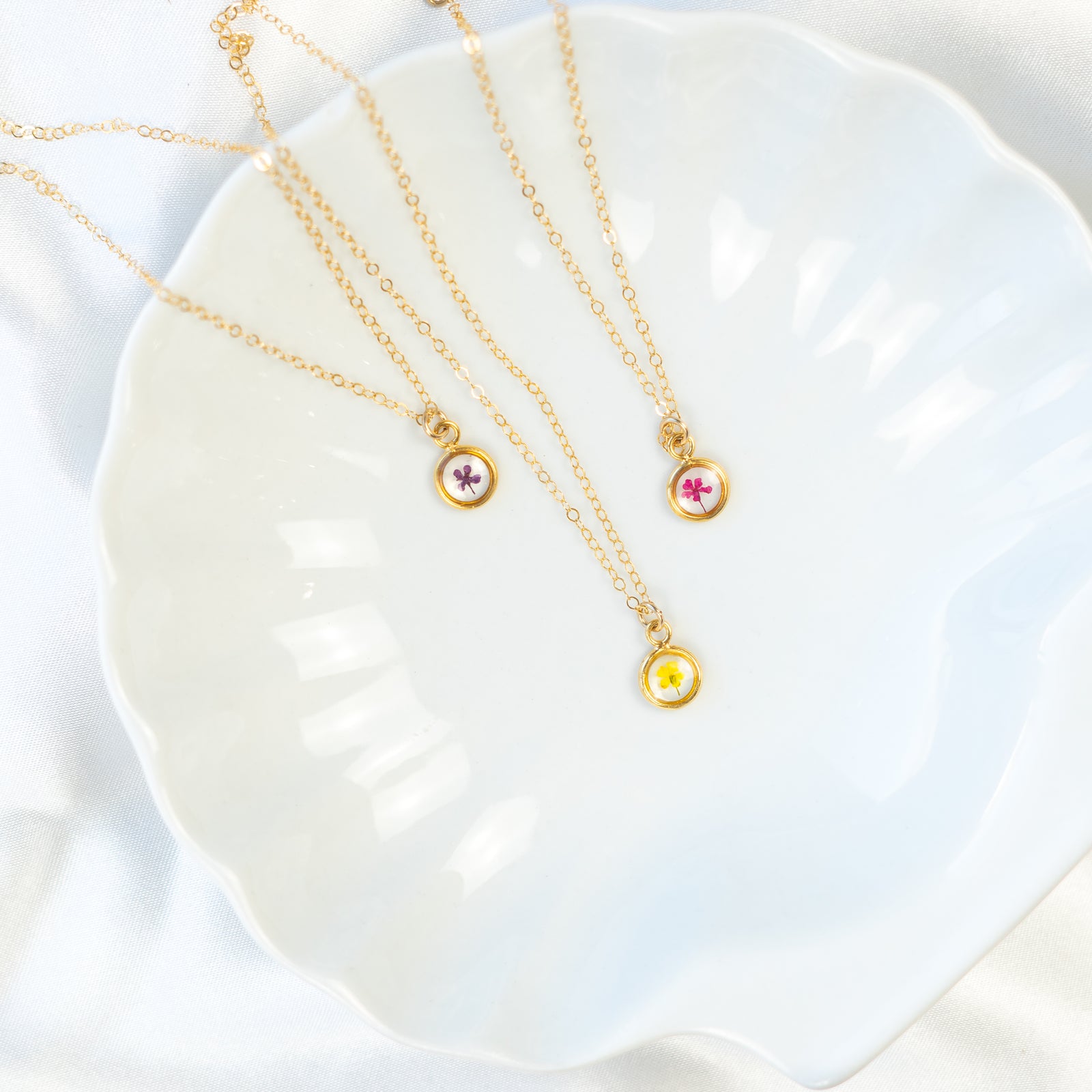 Three 18K gold plated Pressed Floral birth flower mini necklaces on a white textured background