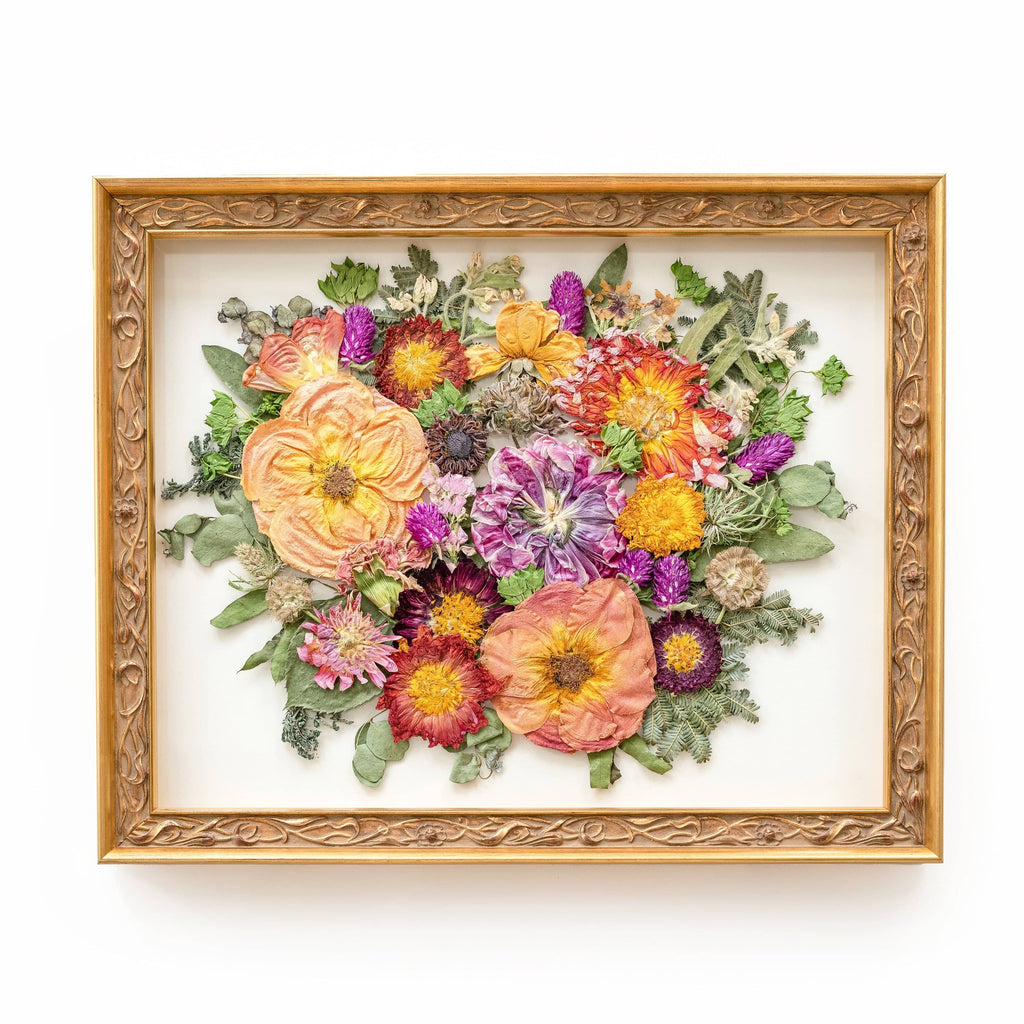A floral antique gold frame adorned with preserved flowers in a captivating arrangement. Radiant red dahlias take center stage, their vibrant petals commanding attention. Graceful purple tulips and delicate pink roses complement the dahlias, adding layers of color and texture. The ornate gold frame enhances the regal beauty of the preserved flowers, creating a visually stunning composition. This arrangement evokes a sense of romance and elegance, capturing the essence of nature's splendor preserved in time.