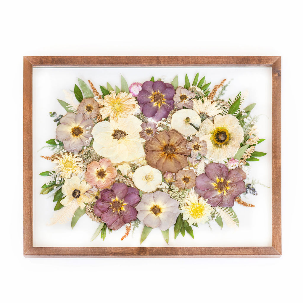 A walnut brown frame adorned with preserved flowers in an enchanting array of colors. Pure white roses, their petals pristine and delicate, mingle with vibrant purple and deep maroon roses. The contrasting hues create a visually striking composition within the frame. The warm tones of the walnut brown frame provide a rich backdrop, accentuating the beauty of the preserved roses and adding a touch of elegance to the overall arrangement.